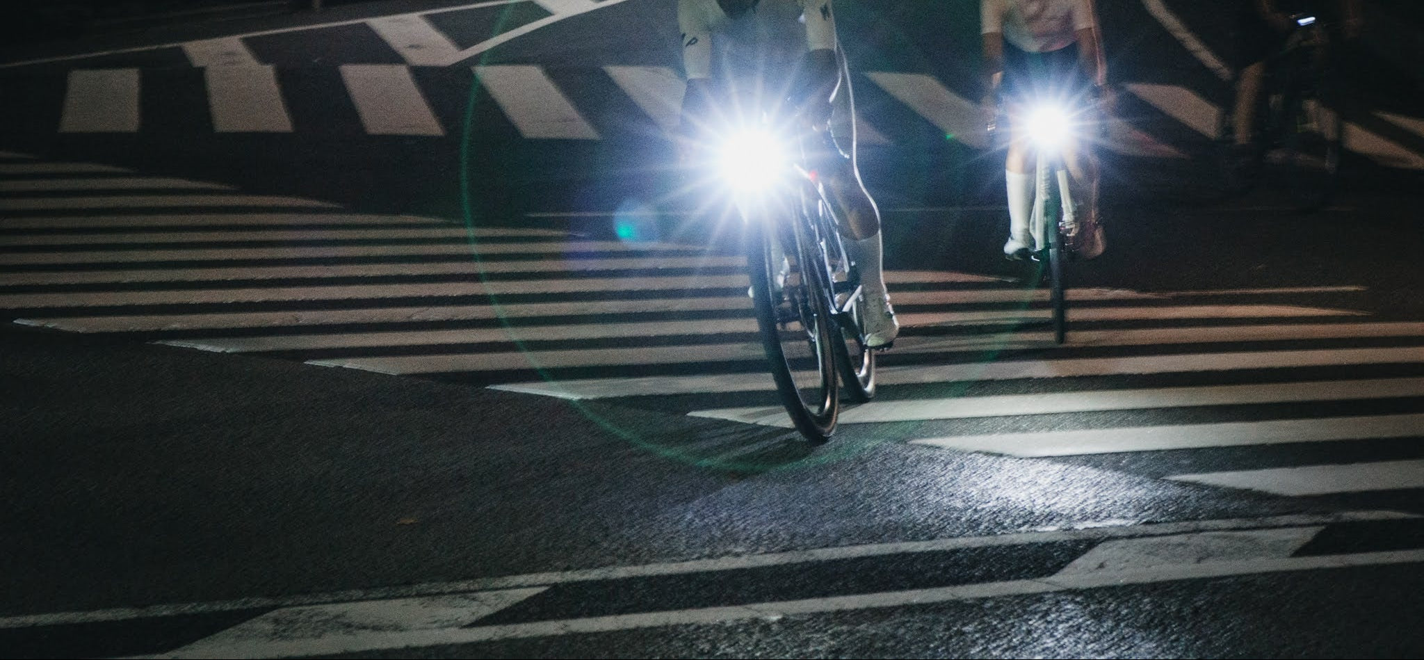 Two cyclists with Volume Bike lights on a zebra crossing at night